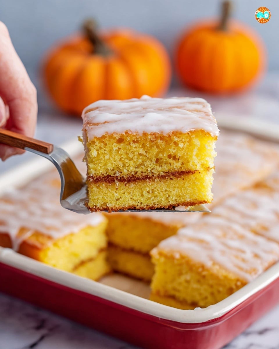 A square piece of yellow cake with a light brown thin filling layer in the center is being lifted by a utensil held by a woman's hand. The cake has two layers of soft, fluffy texture with tiny holes showing its airy nature. The top layer is coated with a shiny, translucent white glaze that slightly drips down the sides. The piece is lifted from a larger, white rectangular baking dish with a red rim, showing more cut cake pieces inside. In the background, there are two small orange pumpkins blurred out, and the scene has a white marbled surface. photo taken with an iphone --ar 4:5 --v 7
