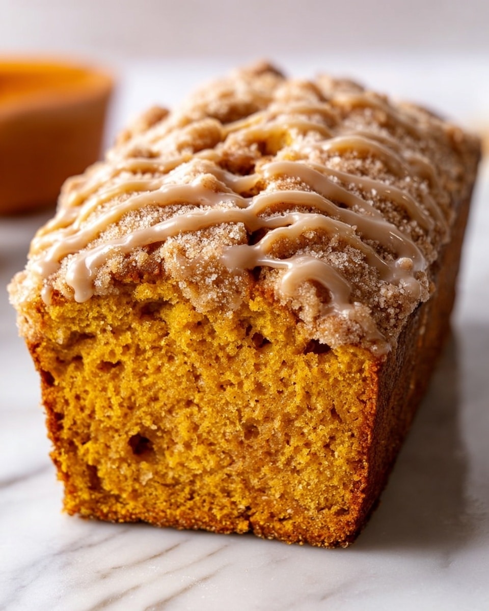The image shows a close-up of a single loaf slice of pumpkin bread with a soft, moist orange-brown inside texture, and a thick, crumbly top layer. The top crust is sprinkled with a powdery streusel and drizzled with a smooth light-brown glaze in a wavy pattern. The bread is placed on a white marbled surface with soft natural light highlighting the textures. Photo taken with an iphone --ar 4:5 --v 7