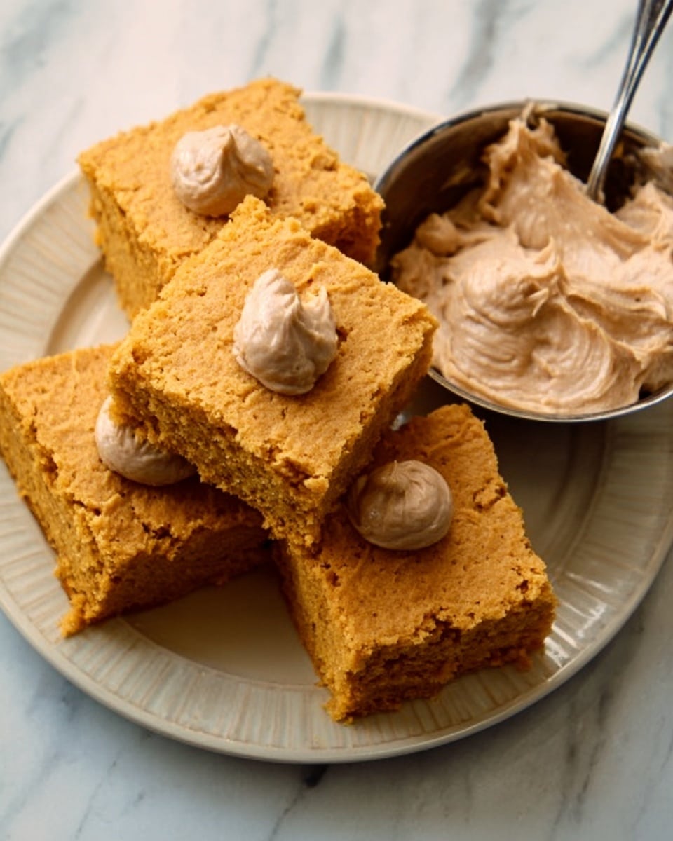 A stack of four square pieces of moist, golden-brown cake with slightly rough texture is shown on a white plate with a soft yellow tint. Each cake piece has a swirl of light brown creamy frosting on top, smooth and soft in texture, with the swirls sitting on top of the cake layers. The background surface is a white marbled texture. Photo taken with an iphone --ar 4:5 --v 7