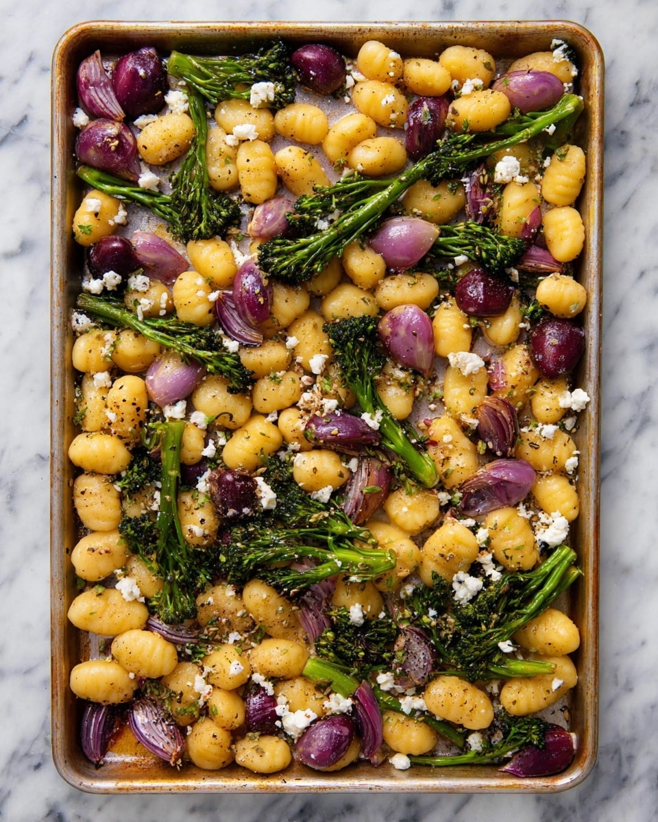 A baking tray filled with a single layer of cooked gnocchi, some are pale yellow and others are purplish-red, mixed evenly with bright green broccolini pieces. Sliced red onions with a light purple color are spread throughout the tray. Small white crumbles of cheese are scattered on top, adding contrast. The vegetables and gnocchi have a slight golden browned tint, showing they are roasted, and there are flecks of black pepper and herbs sprinkled over everything. The tray sits on a white marbled surface. photo taken with an iphone --ar 4:5 --v 7