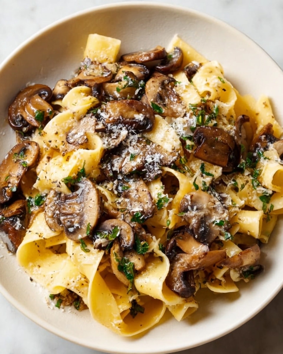 The dish shows a white plate filled with wide, flat pasta noodles in a light golden yellow color, layered evenly across the plate. On top of the pasta are medium to dark brown cooked mushrooms with a slightly shiny texture, mixed with bits of green herbs scattered throughout. The dish is lightly sprinkled with grated white cheese, adding a fine, powdery layer on the noodles and mushrooms. The setting includes a white marbled surface under the plate. The image is clear and close up, showing detail in the textures of the pasta and mushrooms. Photo taken with an iphone --ar 4:5 --v 7