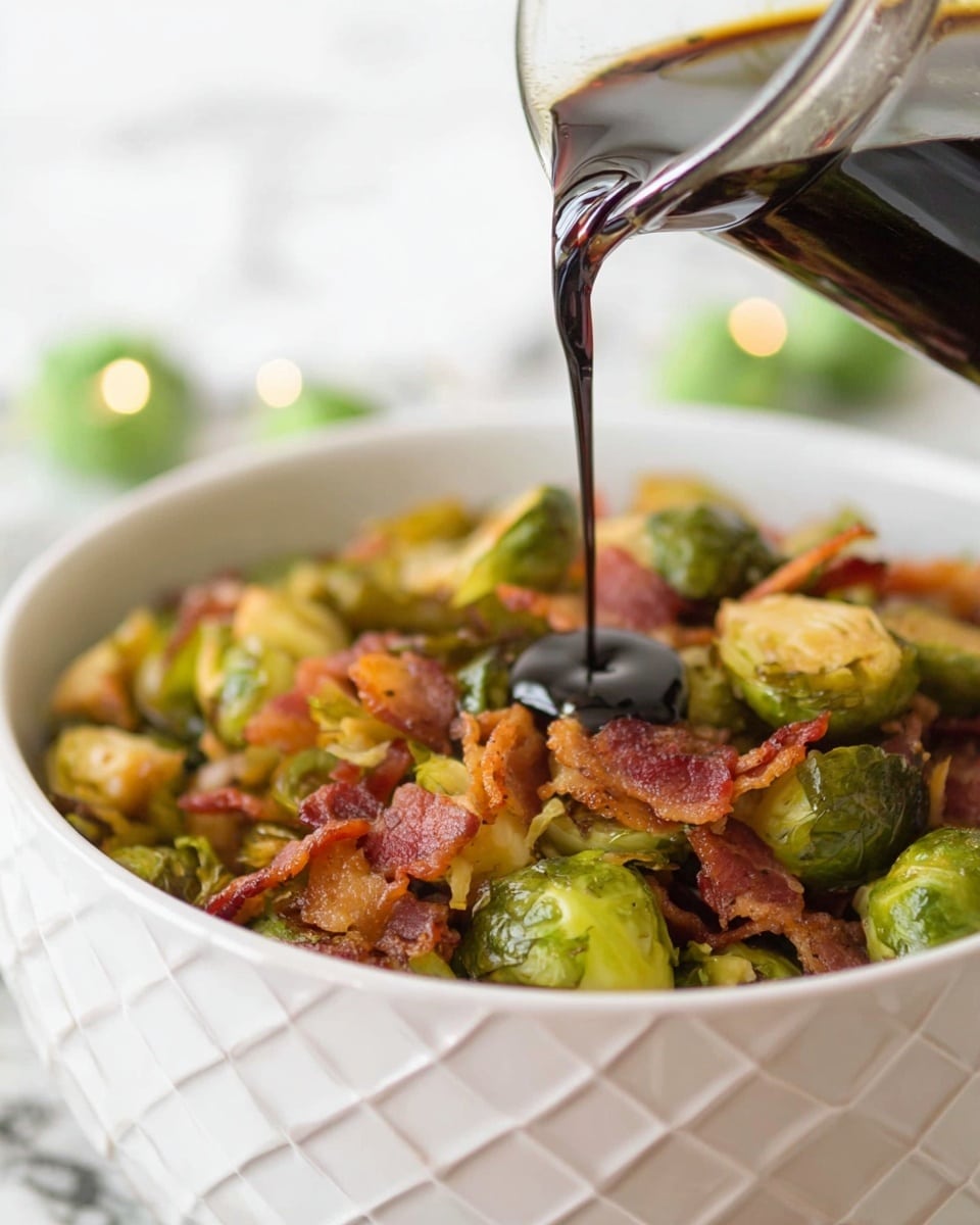 A close-up of a white bowl filled with roasted brussels sprouts and crispy bacon pieces, showing a mix of green, golden-brown, and reddish tones with a texture that looks crunchy and tender. Above the bowl, a dark sauce is being poured from a clear glass container with a diamond pattern, the liquid shiny and thick as it falls onto the vegetables. The background is soft with a white marbled texture, giving a clean and bright look. photo taken with an iphone --ar 4:5 --v 7
