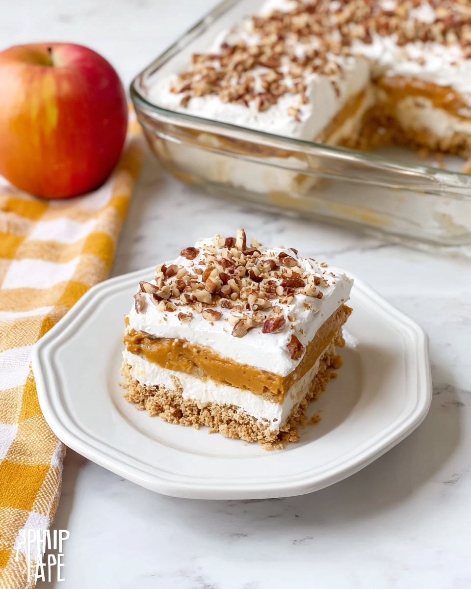 A square piece of layered dessert sits on a white plate with subtle scalloped edges, placed on a white marbled surface. The dessert has three visible layers: the bottom layer is a light brown crumbly crust, the middle layer is a smooth, tan pumpkin filling, and the top layer is a thick white whipped cream sprinkled with chopped pecans. Behind the plate is a rectangular glass dish holding more of the same dessert with the same three layered look and pecan topping. To the left of the plate is a red and yellow apple resting on a folded yellow and white checkered cloth. Photo taken with an iphone --ar 4:5 --v 7
