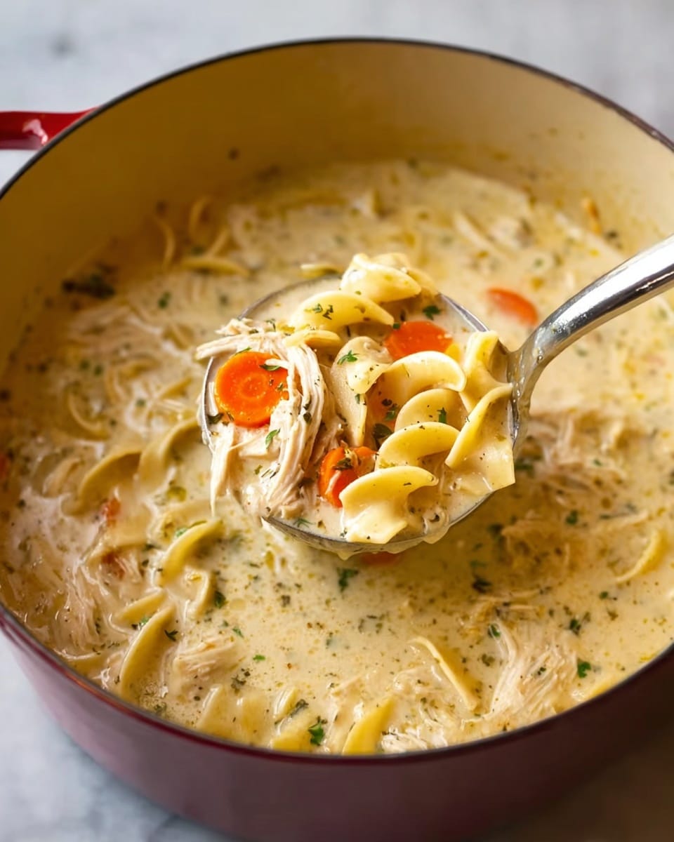 A close-up view of a white ladle lifting creamy chicken noodle soup from a white pot. The soup has three main visible layers: a thick, creamy broth with a pale yellow color and specks of herbs spread throughout; shredded pieces of white chicken meat scattered around; and yellow egg noodles and bright orange carrot slices, layered evenly throughout the soup. The pot rests on a white marbled surface. photo taken with an iphone --ar 4:5 --v 7
