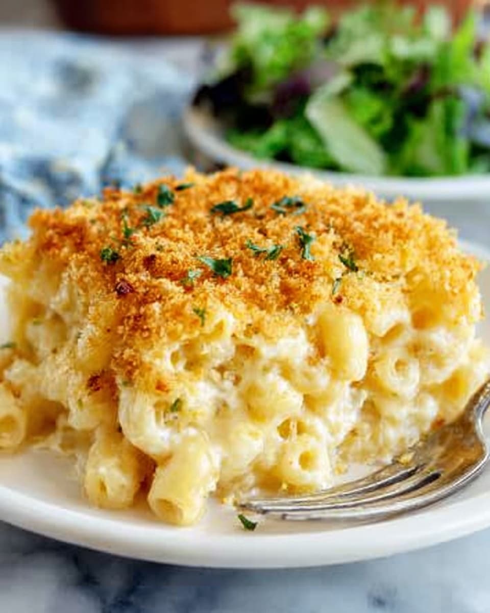 A white plate holds a single square piece of macaroni and cheese with three visible layers: the bottom layer is soft yellow pasta, the middle layer is creamy white cheese sauce that oozes slightly, and the top layer is golden brown toasted breadcrumbs with a crunchy texture and small green herb bits scattered sparsely. The plate rests on a white marbled surface, and a fork is placed to the right of the plate. In the background, there is a blurred green salad visible, adding a touch of freshness to the scene. Photo taken with an iphone --ar 4:5 --v 7