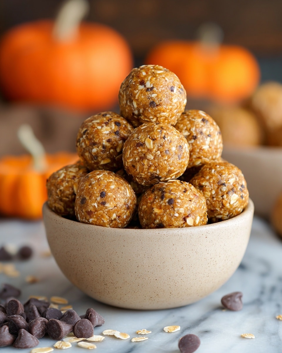 A beige bowl filled with a pyramid stack of round, golden-brown energy balls that have a rough texture with visible oats and small dark specks, sitting on a white marbled surface with some scattered rolled oats and dark brown chocolate chips around it. In the background, there are blurred orange pumpkins that add a warm, autumn feel to the image. Photo taken with an iphone --ar 4:5 --v 7