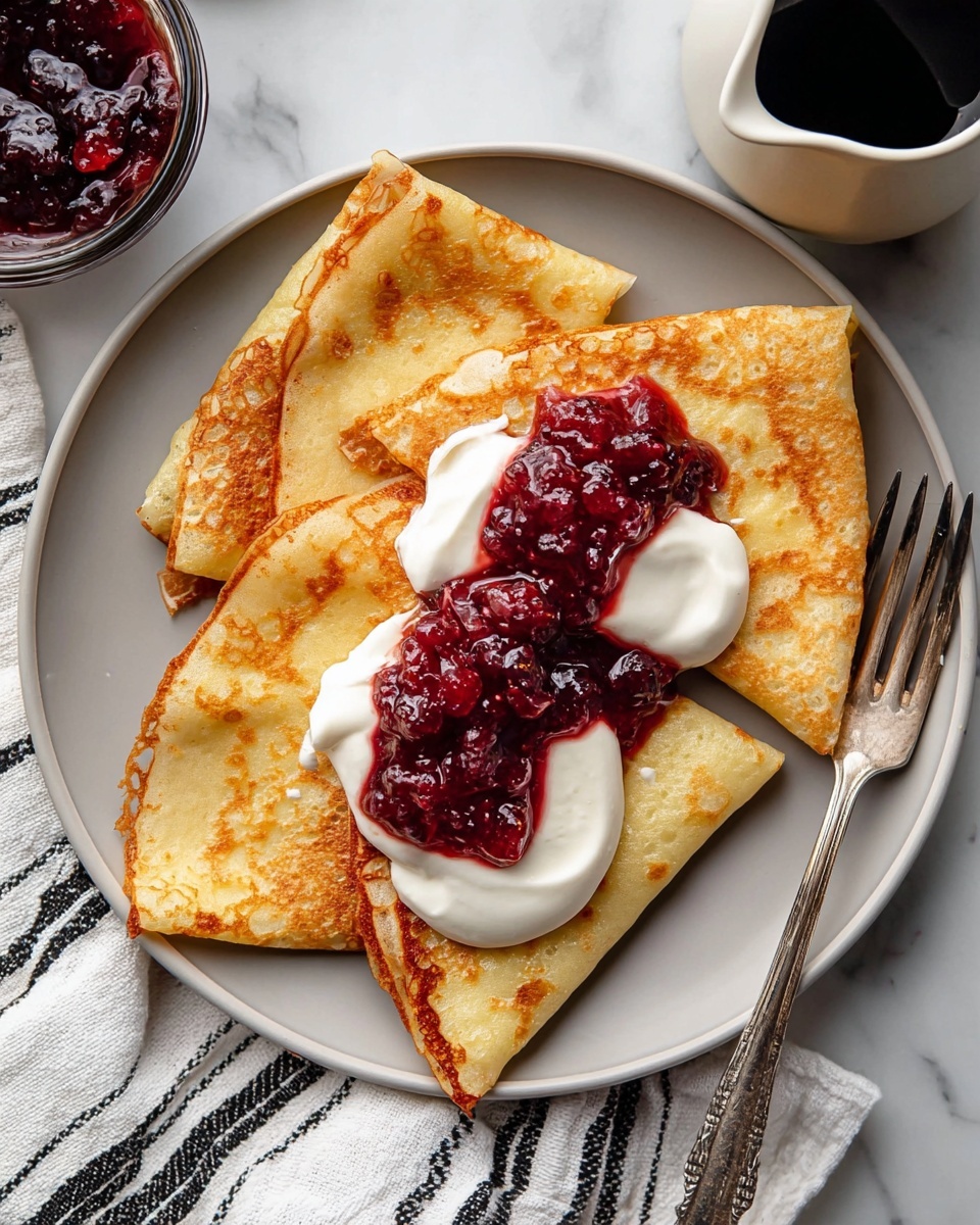 A white plate holds three folded golden-brown crepes with a slightly crispy texture around the edges, arranged in a fan shape. On top, there is a thick dollop of smooth, white cream, crowned with a generous scoop of glossy, deep red berry jam that has visible fruit pieces and a slightly chunky texture. The plate rests on a white marbled surface next to a fork with a simple handle design. Nearby, there is a white cloth with thin black stripes and a white jug filled with dark syrup. Photo taken with an iphone --ar 4:5 --v 7