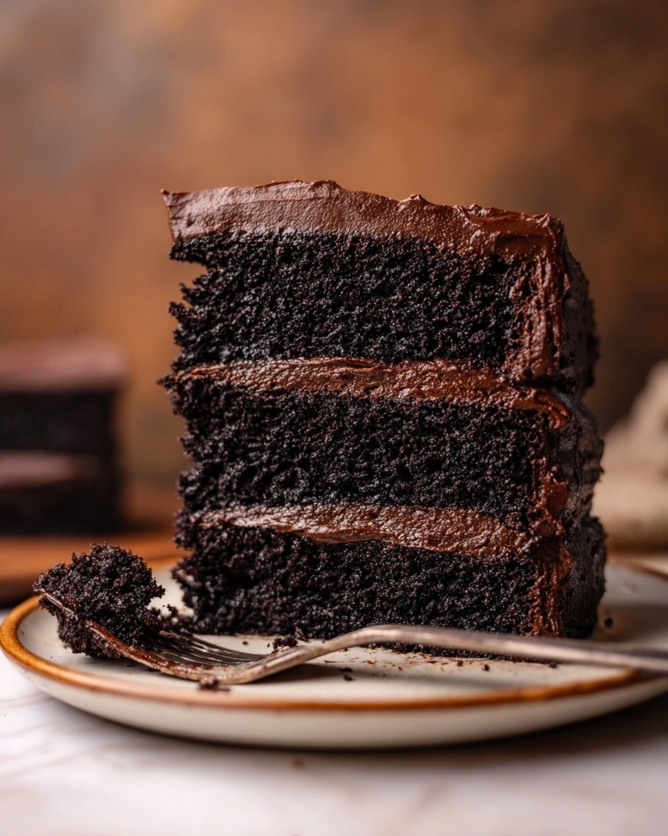 A slice of chocolate cake is cut into three thick layers stacked on a white plate with brown rim details, each layer dark brown and moist with a rough texture. Between each cake layer is a rich, smooth, thick spread of dark chocolate frosting, and the top layer is fully covered with the same dark chocolate frosting spread unevenly, showing some texture. Next to the cake on the plate is a bit of cake crumb and frosting, with a silver fork partially visible behind the cake. The background is softly blurred in warm brown tones, and the scene is set on a white marbled textured surface. photo taken with an iphone --ar 4:5 --v 7