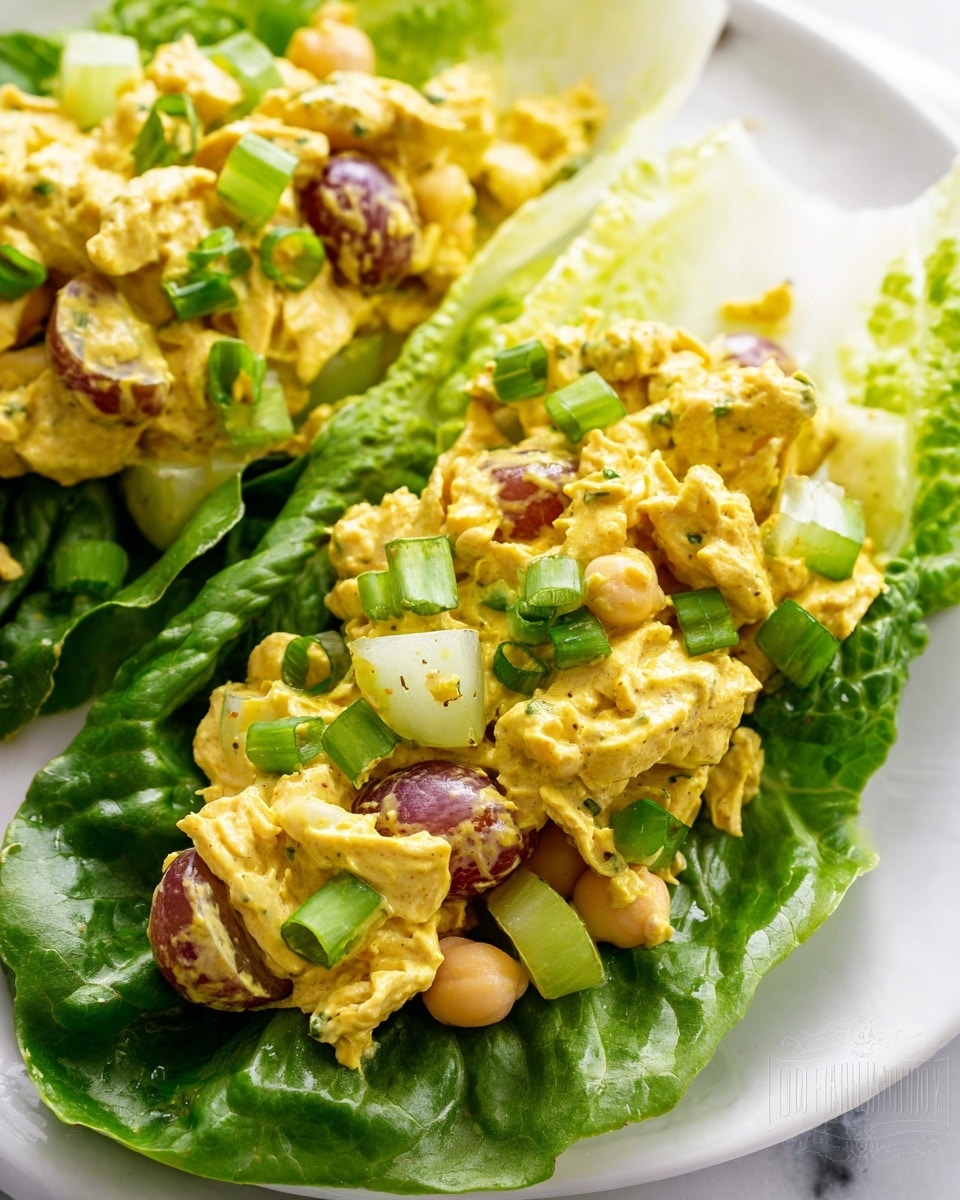 A close-up view of a white plate holds fresh green romaine lettuce leaves forming a base layer. On top, there is a generous amount of creamy yellow chicken salad mixed with small pieces of red grapes, light green celery slices, and pale chickpeas. The chicken salad has a thick, slightly uneven texture, coated in a mustard-yellow dressing. The dish is garnished with small green onion slices scattered over the top. The background shows a white marbled texture. photo taken with an iphone --ar 4:5 --v 7