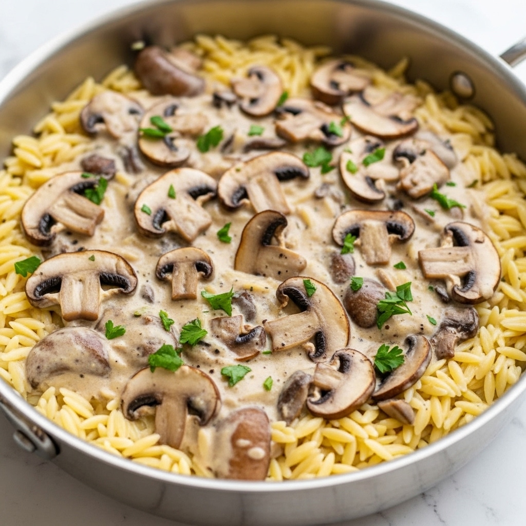 A close-up of a white bowl filled with creamy orzo pasta mixed with sautéed brown mushrooms and bright green spinach leaves, showing a creamy sauce coating the pasta. The orzo is light beige and soft, with small flecks of black pepper and grated cheese scattered on top. A wooden spoon scoops some of the mixture, revealing the rich texture of the sauce with pieces of mushrooms and spinach layered throughout. To the side, a block of pale yellow cheese with some grated cheese next to it is slightly visible, all set on a white marbled surface. photo taken with an iphone --ar 4:5 --v 7